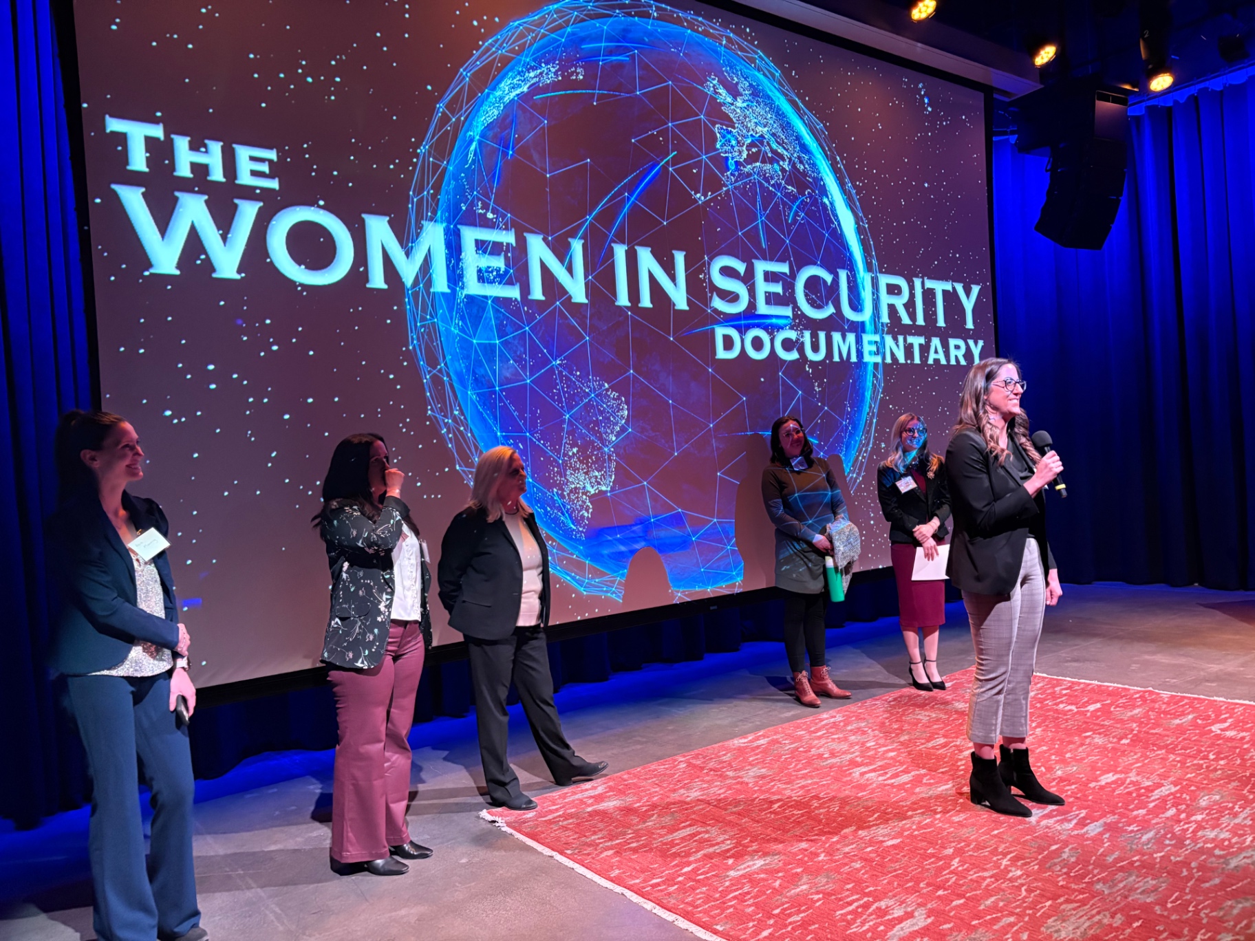 A speaker introducing a panel before a seated audience at an industry event.