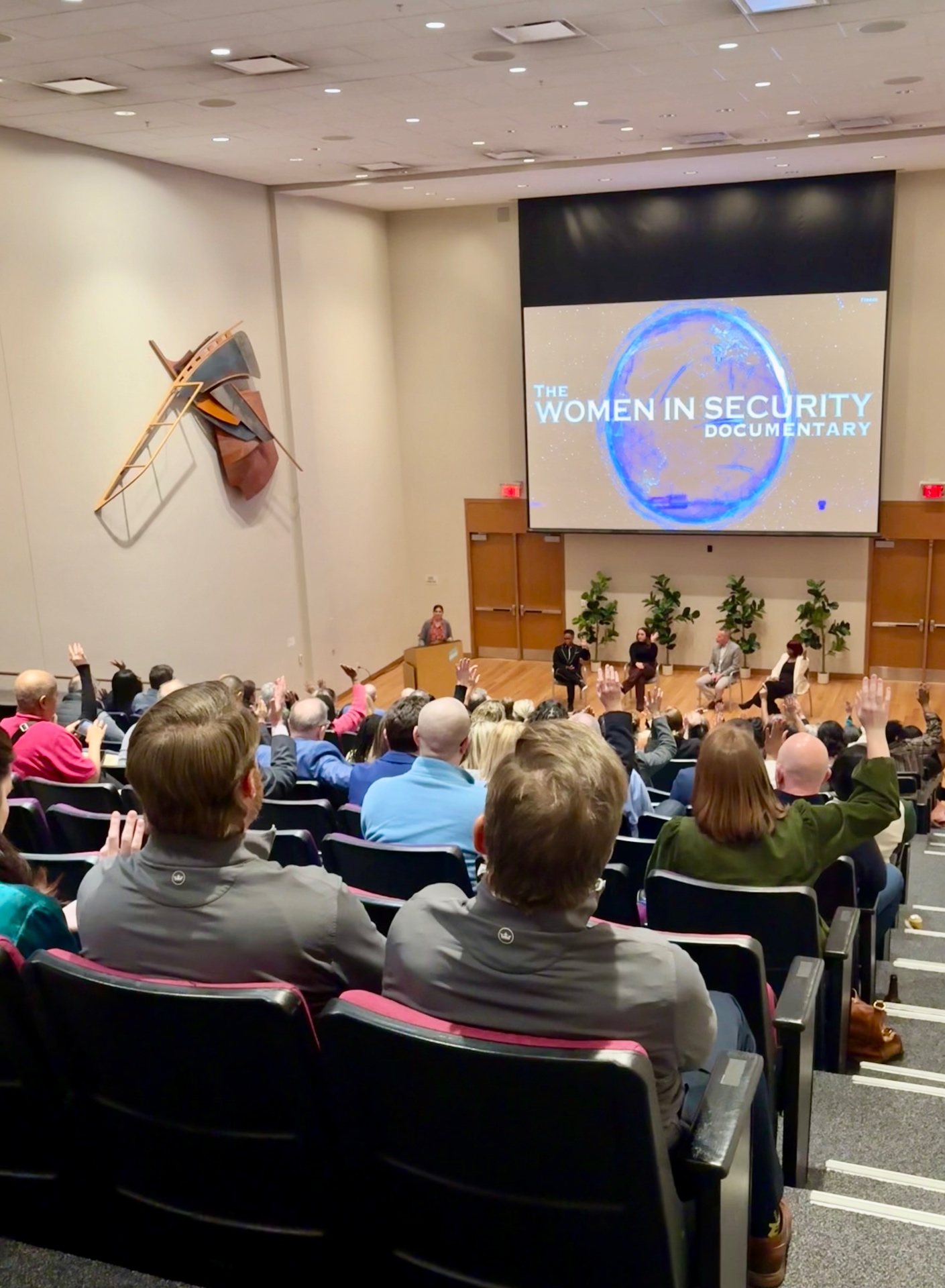 An audience with hands raised during a question and answer session after a screening.