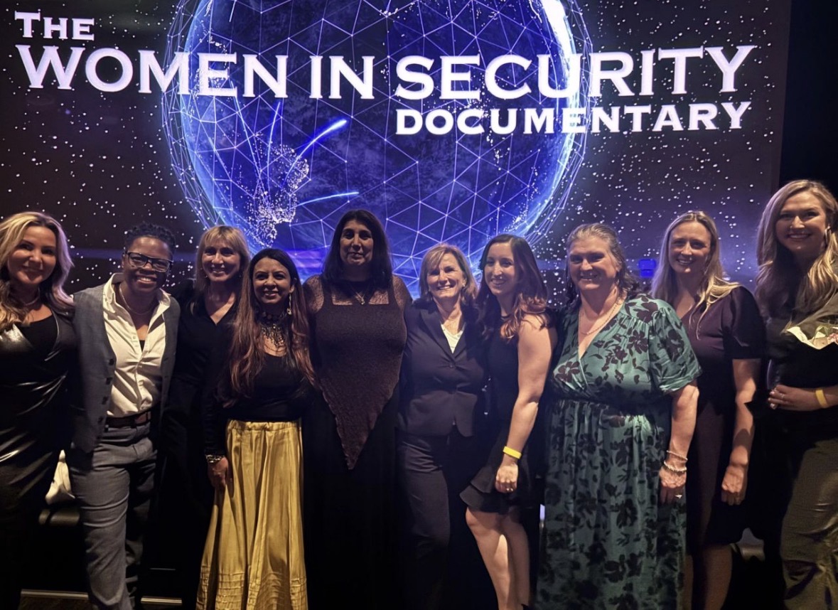Women featured in The Women In Security Documentary gathered on a cinema stage in front of the film's title screen.